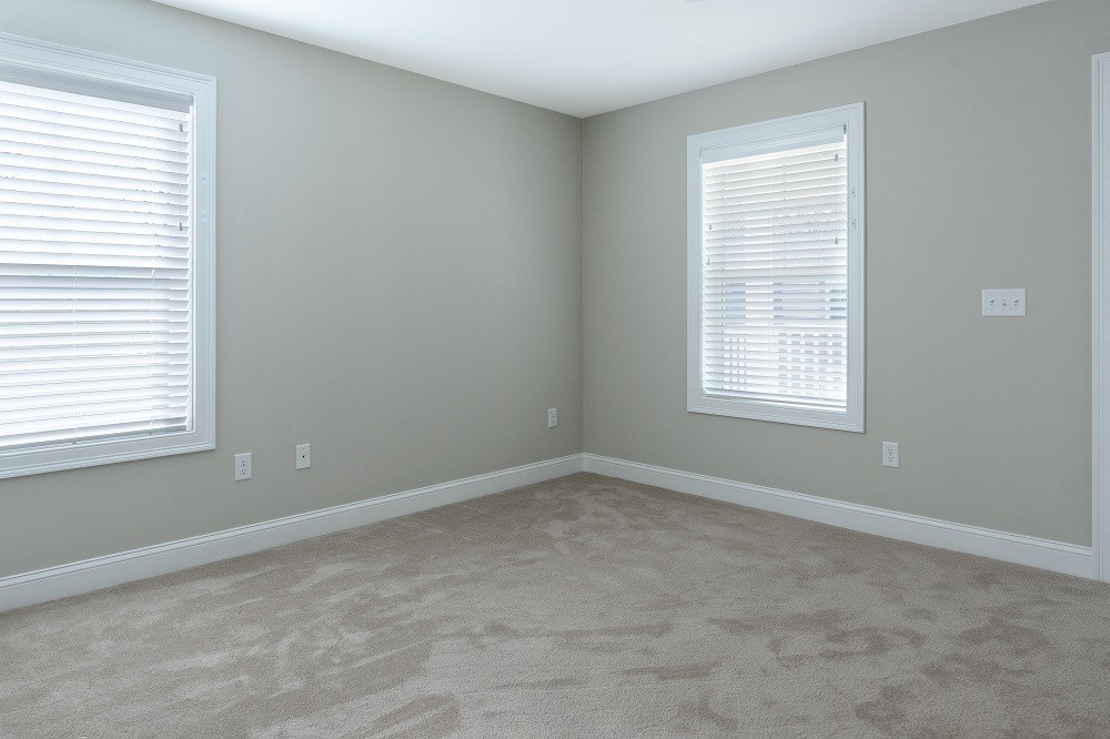 an empty room with carpet and two windows
