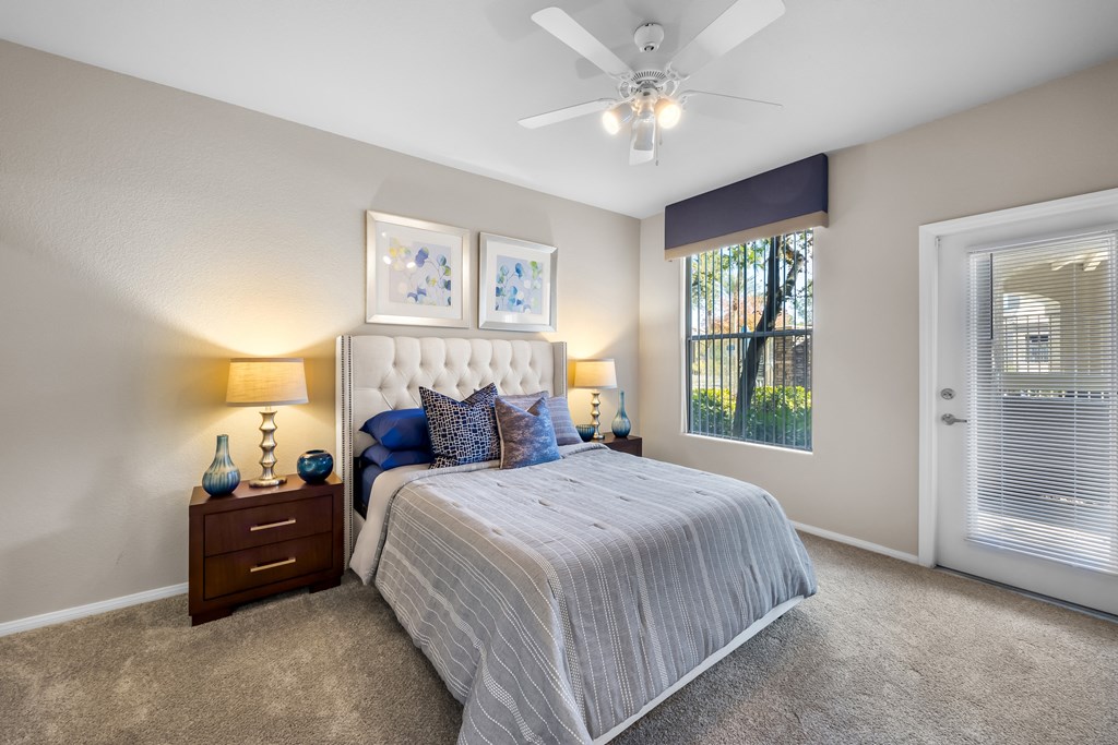 A bedroom with a large bed, a ceiling fan, and two nightstands with lamps. at The Equestrian by Picerne Apartments, Henderson