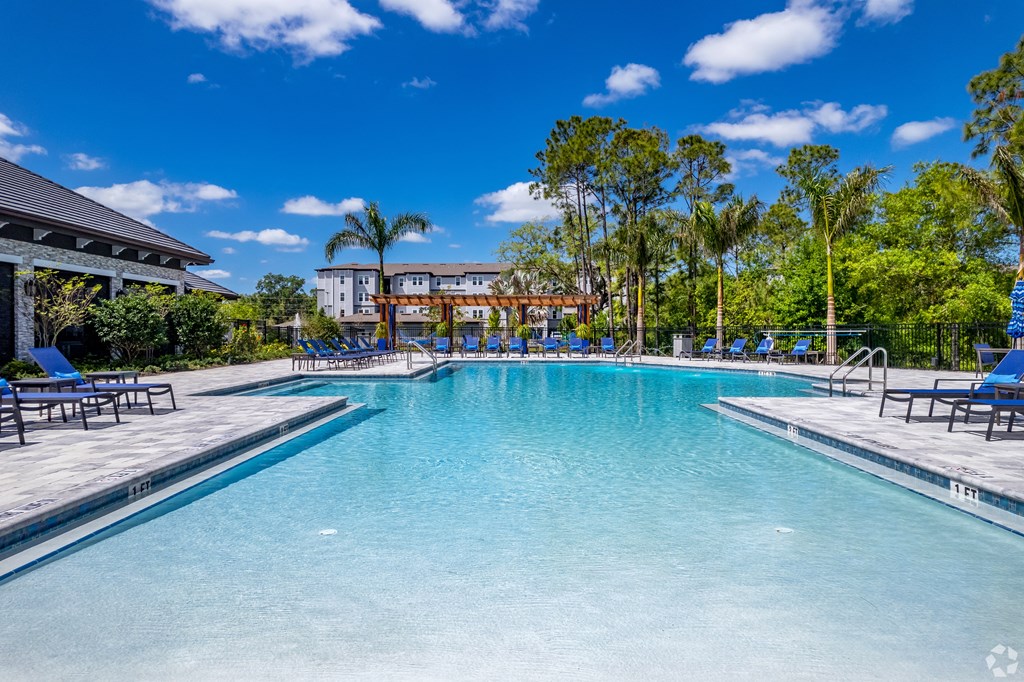 a large swimming pool with chaise lounge chairs and a building in the background at The Oasis at Manatee River, Bradenton, FL, 34211