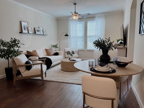 A living room with a white couch, a wooden chair, a round table with a vase on it, and a potted plant.