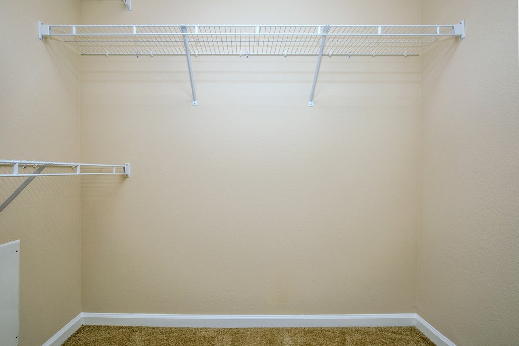 a walk in closet in an empty room with white shelves