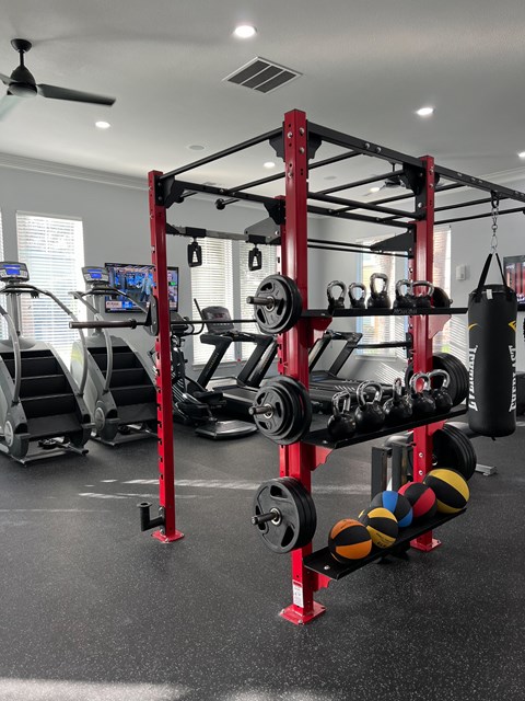 A red and black weightlifting rack with weights and a punching bag in a well lit room.