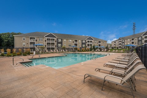 A swimming pool surrounded by sun loungers in front of apartment buildings.