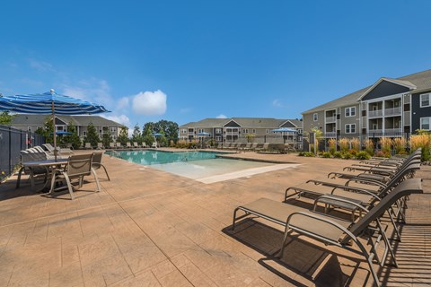 A pool surrounded by chairs and umbrellas with apartment buildings in the background.