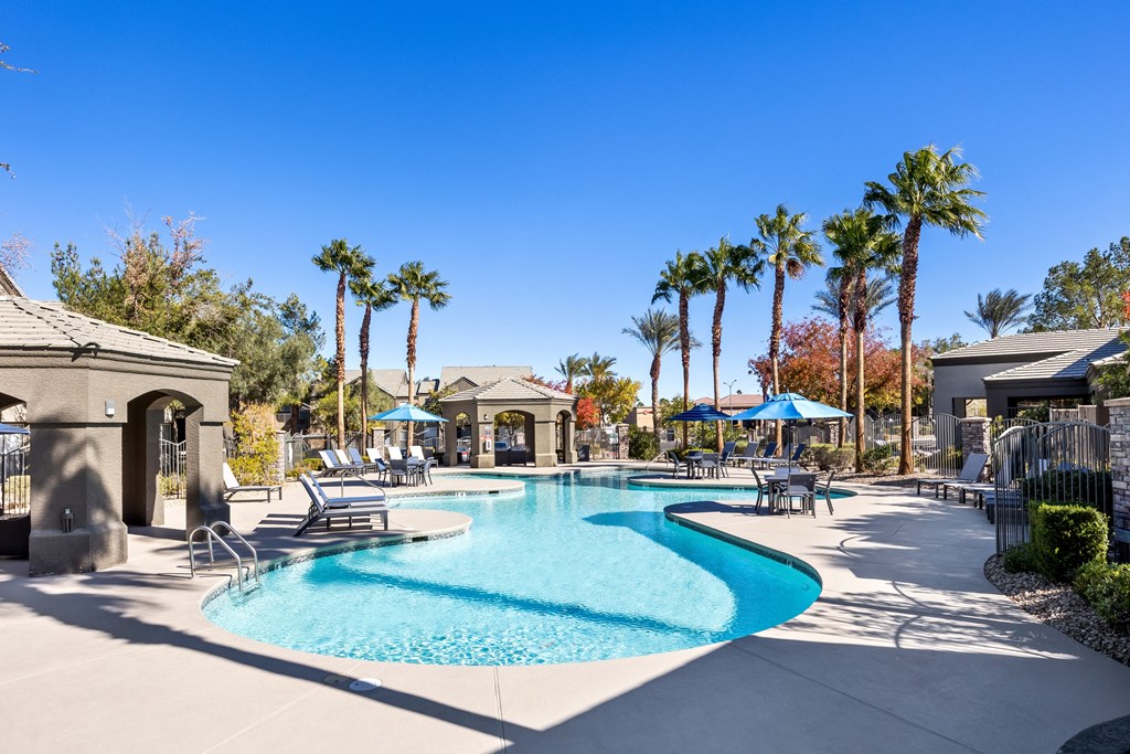A large swimming pool surrounded by palm trees and lounge chairs. at The Equestrian by Picerne Apartments, Henderson 89052