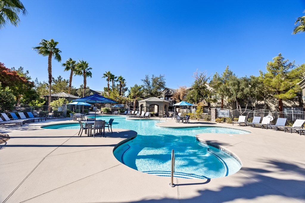 A large swimming pool surrounded by palm trees and lounge chairs. at The Equestrian by Picerne Apartments, Henderson, NV, 89052