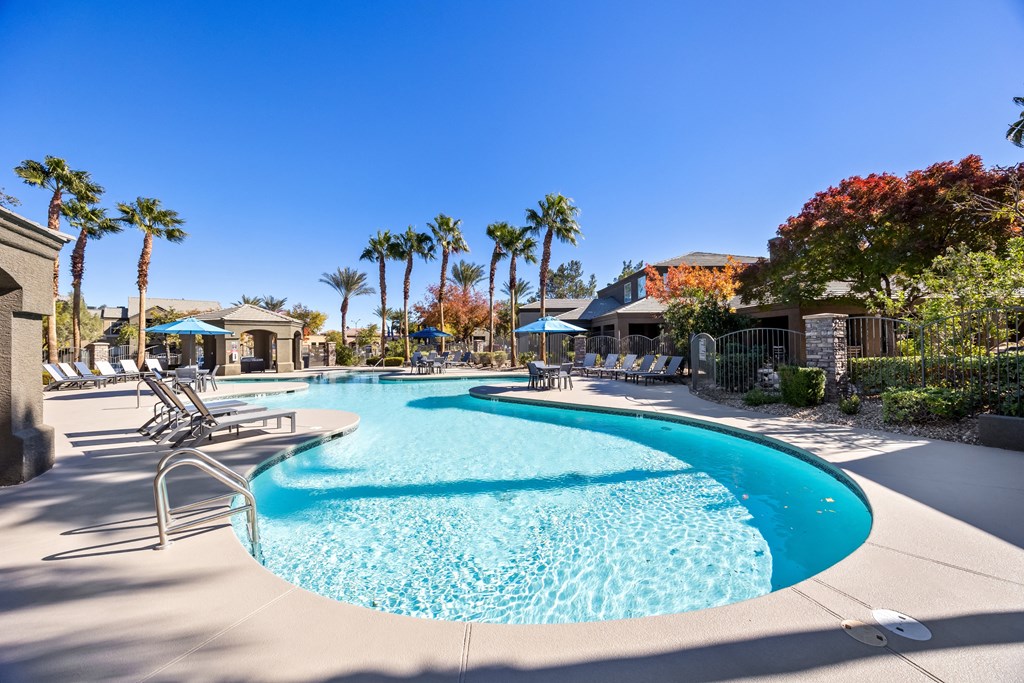 A large swimming pool surrounded by palm trees and lounge chairs. at The Equestrian by Picerne Apartments, Henderson 89052