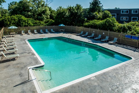 A small pool surrounded by a wooden fence and lounge chairs.