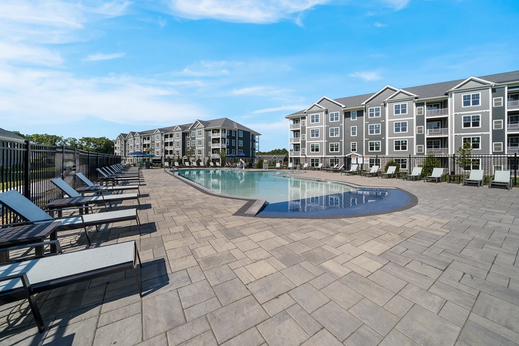 a swimming pool with lounge chairs around it in front of an apartment building