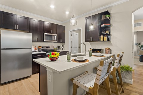 A kitchen with a refrigerator, microwave, and a counter with a bowl of fruit on it.