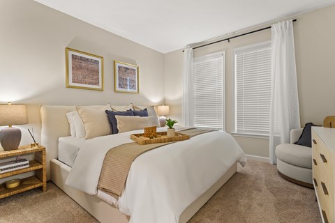 A bedroom with a large bed and a window with white curtains.