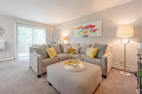 A living room with a grey couch, a white ottoman, and a painting on the wall.