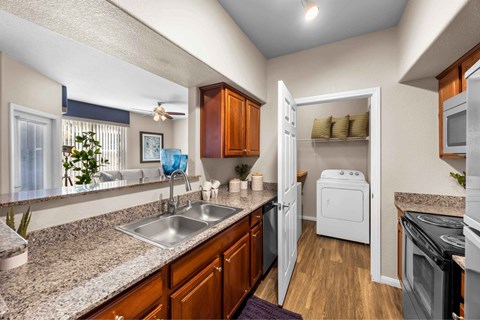 A kitchen with a white dishwasher and wooden cabinets. at The Belmont by Picerne, Las Vegas