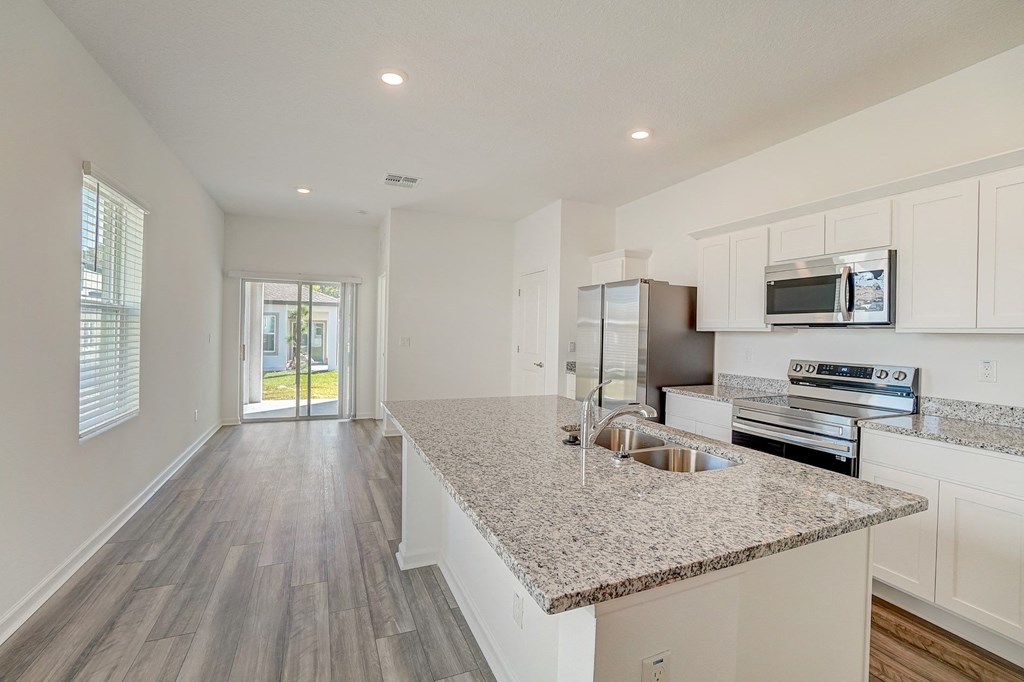 Oak floor plan kitchen with granite counters, a kitchen island, and stainless steel appliances at Beacon at Clinton Corners in Dade City, FL