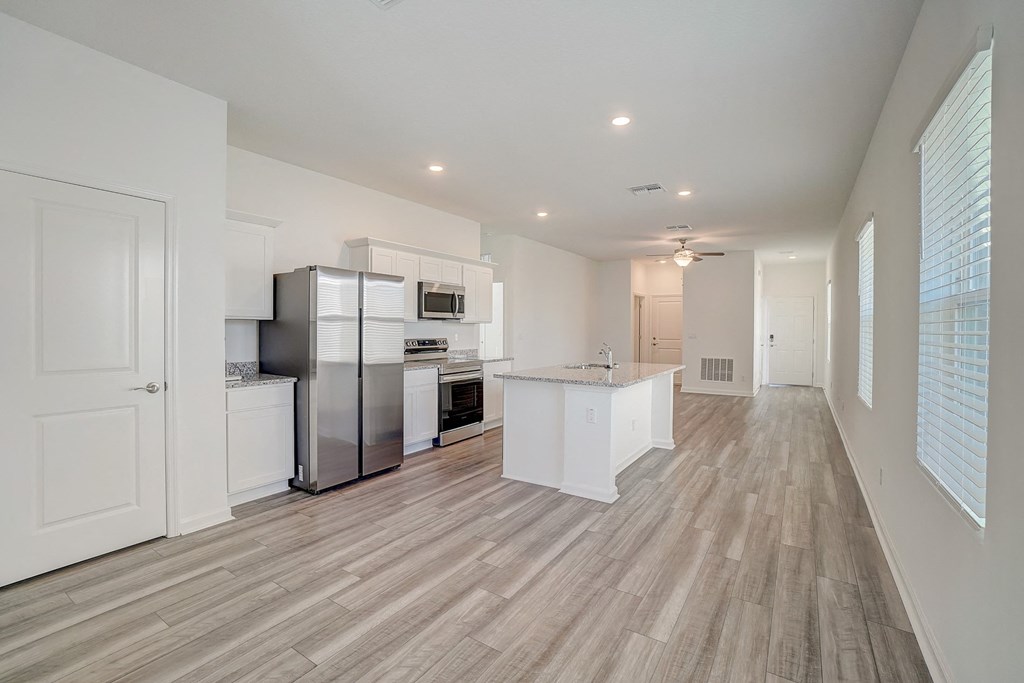 Open kitchen with white cabinets, a kitchen island, and stainless steel appliances of the Oak floor plan at Beacon at Clinton Corners in Dade City, FL