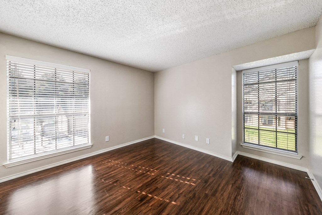 an empty living room with wood floors and two windows