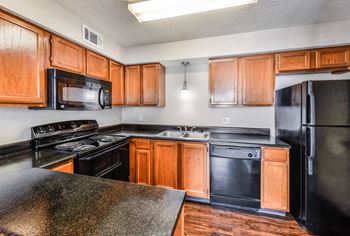 Kitchen with black appliances and wood cabinets at Camino del Sol in Denton, TX