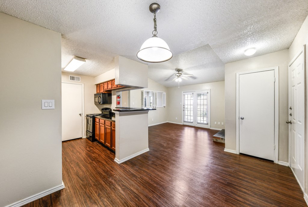 an empty living room and kitchen with wood flooring and a ceiling fan