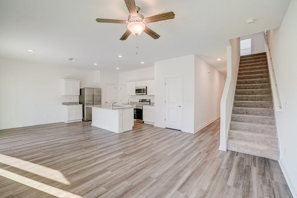 View from living room with ceiling fan to kitchen and stairway up to second floor in the Verbena floor plan at Beacon at Clinton Corners in Dade City, FL