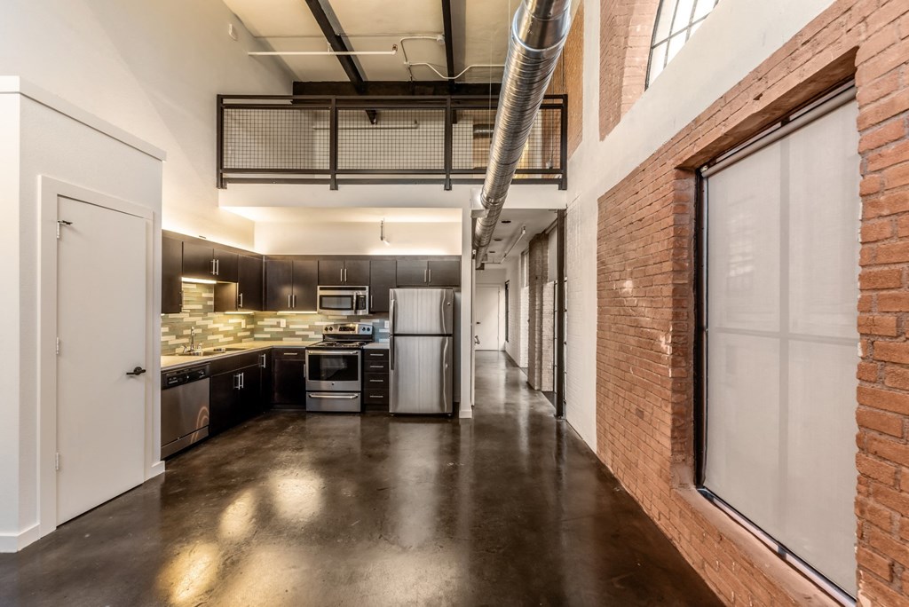3333 Elm Street Lofts studio kitchen with stainless steel appliances, brick accent walls, and a large arched window at Deep Ellum Lofts in Dallas, TX