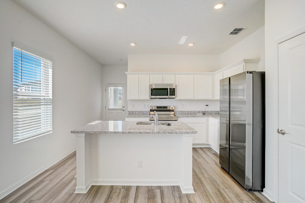Kitchen with white cabinets, granite countertops, and stainless steel appliances in the Elm floor plan at Beacon at Clinton Corners in Dade City, FL