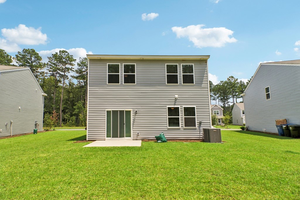 Open grassy area behind the house with clear skies and greenery at Beacon at Ashley River Landing in Summerville, SC