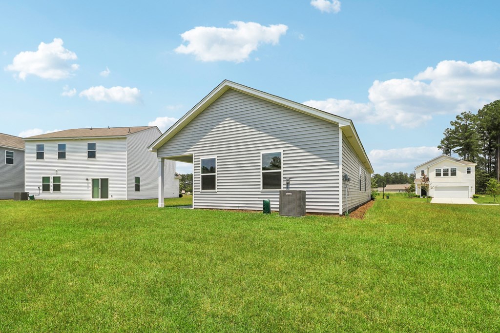 Backyard view of a one-story house with a light gray exterior and a spacious lawn at Beacon at Ashley River Landing in Summerville, SC