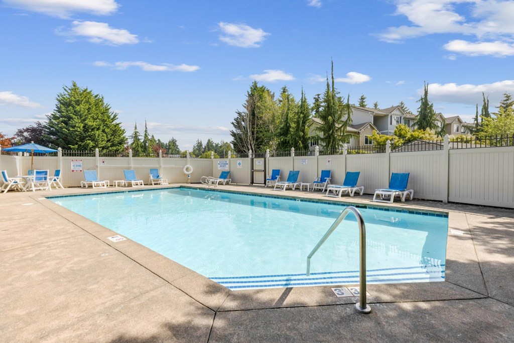 A large swimming pool surrounded by a white fence and blue lounge chairs at Abbey Rowe Apartments in Olympia, WA