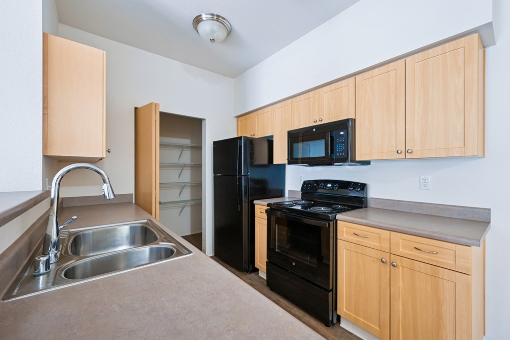 Soho kitchen with black appliances, a pantry closet, and wooden cabinets at Abbey Rowe Apartments in Olympia, WA