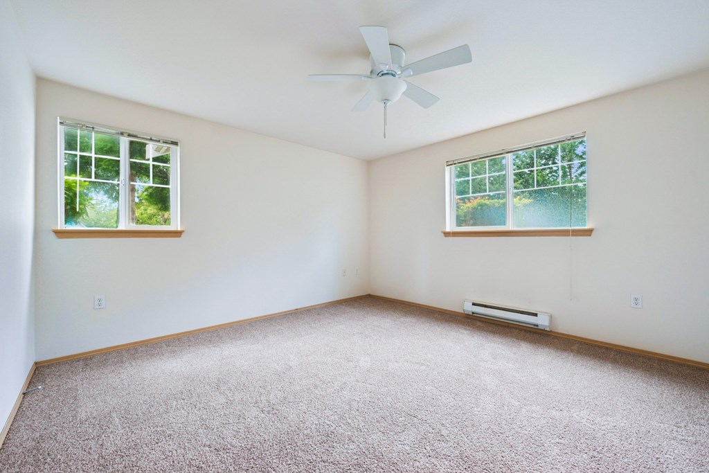 Spacious York bedroom with a carpeted floor, a ceiling fan, and two windows at Abbey Rowe Apartments in Olympia, WA