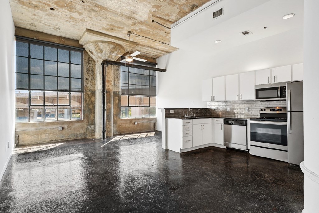Loft kitchen and living space with stainless steel appliances, ceiling fan, and polished concrete floors | Adam Hats Lofts from Deep Ellum Lofts in Dallas, TX