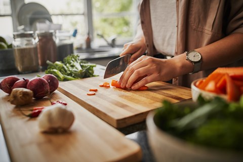 A person is chopping vegetables on a wooden cutting board.