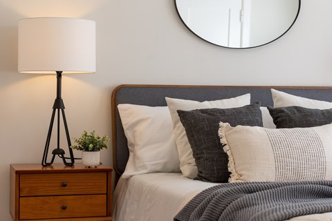 A bedroom with a bed, pillows, a lamp, and a mirror.