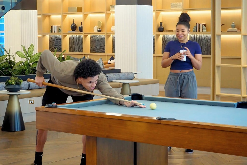 A man is playing pool while a woman watches and drinks coffee at Era Apartments in Denton, TX