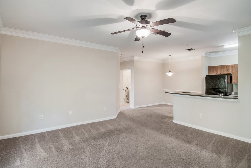 an empty living room with a ceiling fan and a kitchen