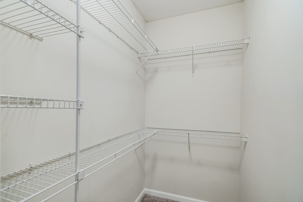 a walk in closet with white walls and glass shelves
