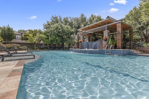 A pool with a wooden deck and a pavilion in the background.