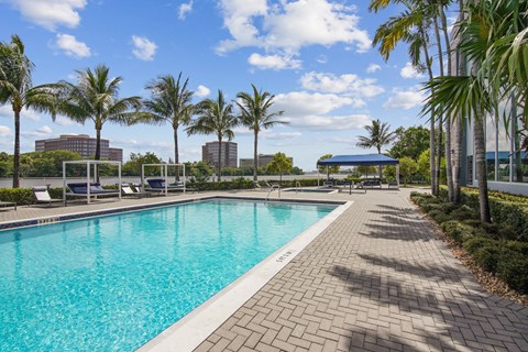 A sparkling swimming pool surrounded by palm trees and brick walkways at Blue Lagoon 7 Apartments in Miami, FL