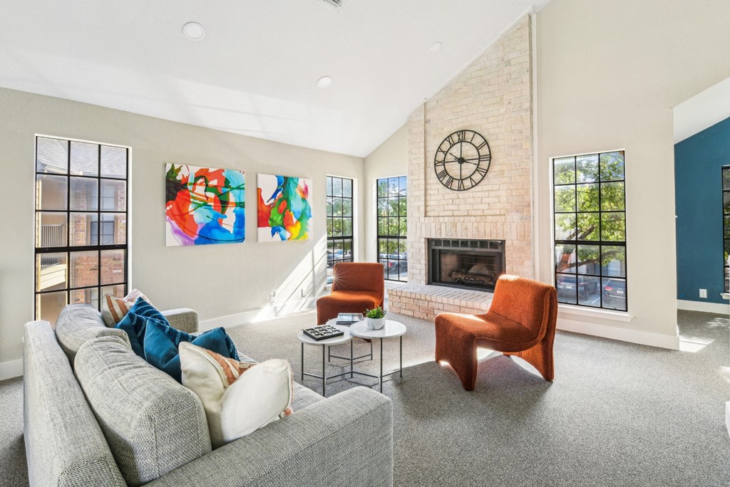 Cozy lounge space in clubhouse with fireplace, couch and orange plush seats at Bandera Crossing apartments in San Antonio, TX
