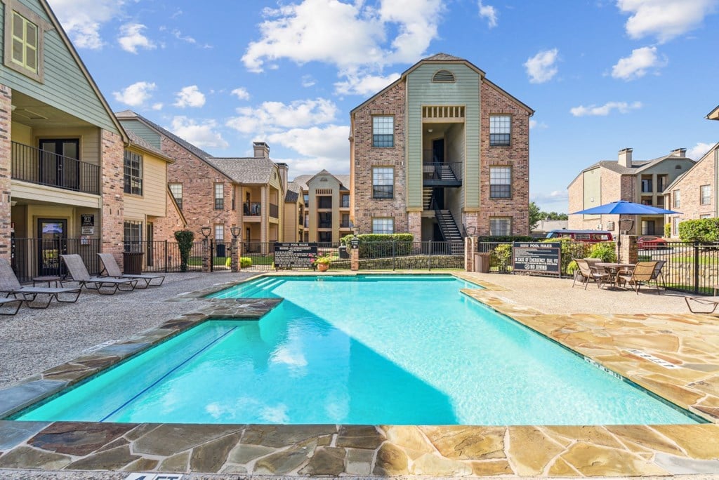 Swimming pool surrounded by apartment buildings with lounge chairs at Bandera Crossing apartments in San Antonio, TX