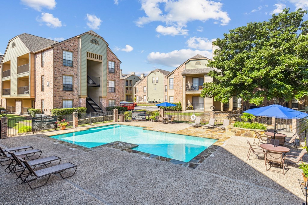 Community pool with lounge chairs surrounded by apartments at Bandera Crossing apartments in San Antonio, TX