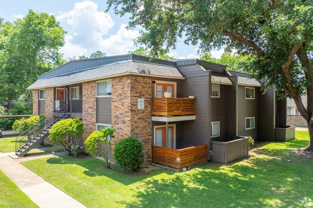 View of apartment building with patio and balcony overlooking lush green space at Bayou Oaks Apartment Homes in Alexandria, LA