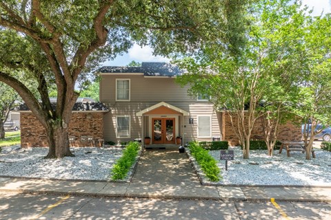 A house with a brown roof and a grey wall is surrounded by trees.