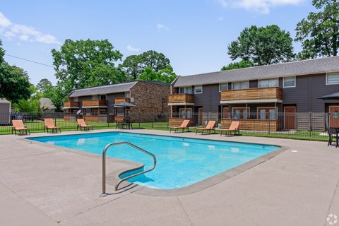 A swimming pool in front of a building with lounge chairs around it.