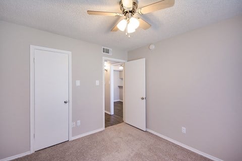 an empty bedroom with a ceiling fan and a door to a hallway