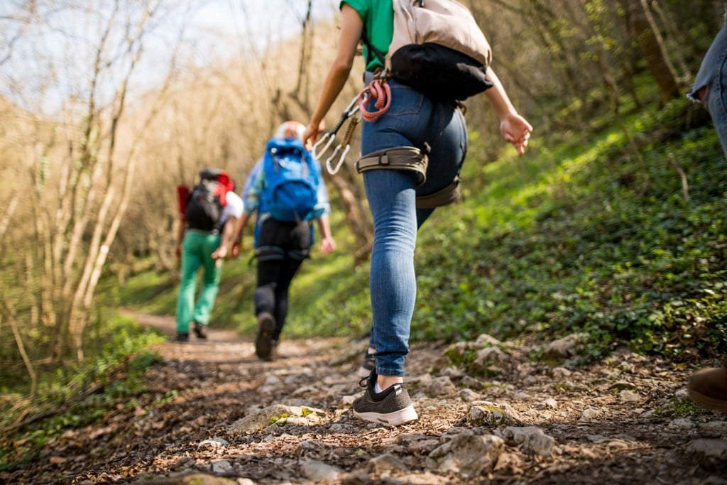 A person in a green shirt and blue jeans is running on a trail in the woods.