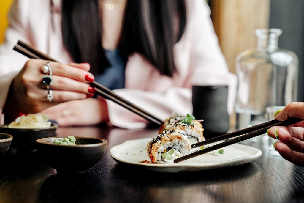 A woman is eating sushi with chopsticks.