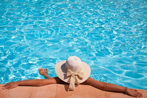 A woman in a hat is relaxing by the pool.