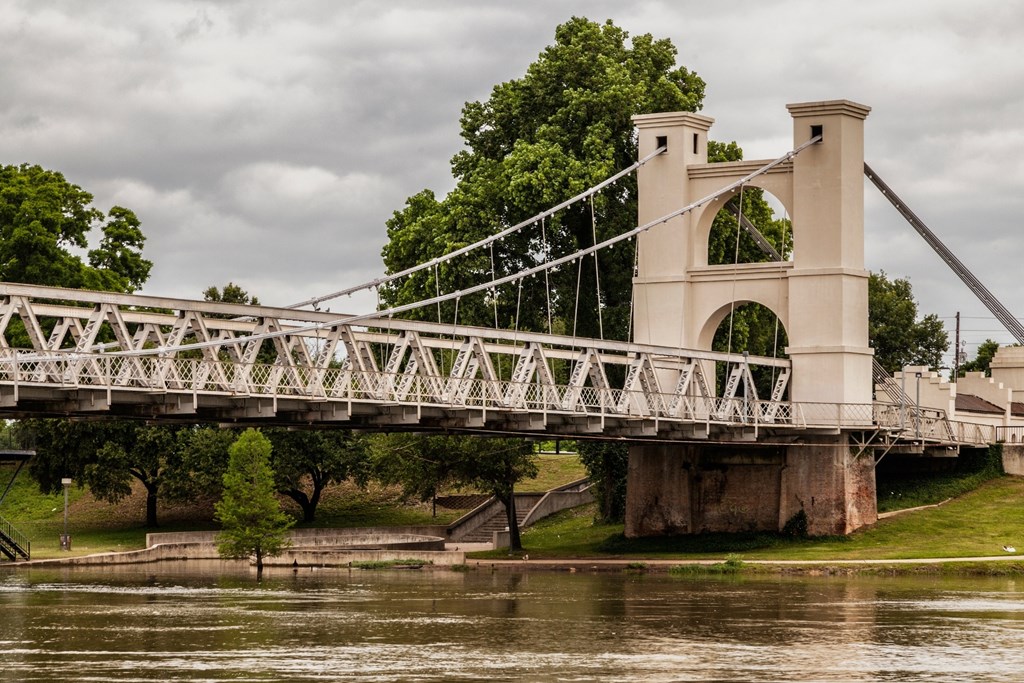 A bridge with a metal structure and two towers spans over a body of water.