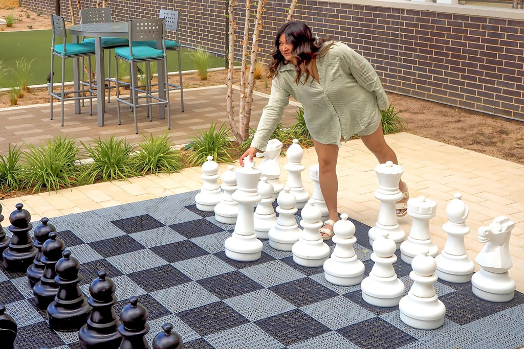 A woman is playing chess on a checkered mat at Era Apartments in Denton, TX